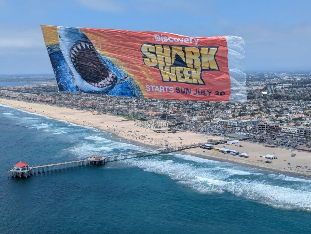 Full-color billboard banner flying over a beach and pier