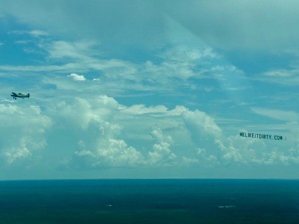 Tow plane pulling a letter banner across a cloudy sky over the coast